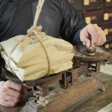 Traditional Asian apothecary worker weighting package Cropped image of traditional Asian apothecary worker putting plummet on scales to weight package with treatment
